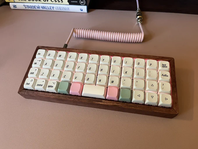 A 40% ortholinear mechanical keyboard with a pink cable and wooden case with white, pink and green keycaps