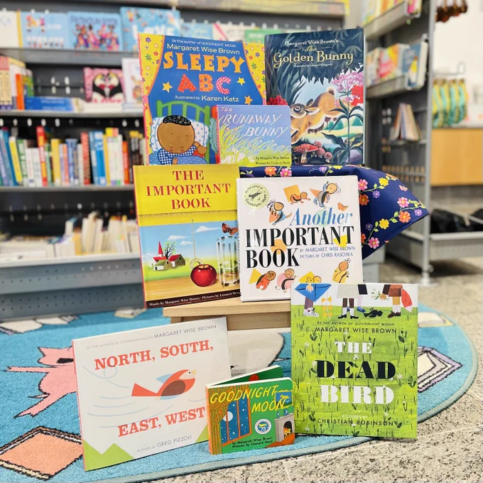 Eight picture books written by Margaret Wise Brown including Goodnight Moon and The Dead Bird are posed on a short wooden bench inside The Carle Bookshop
