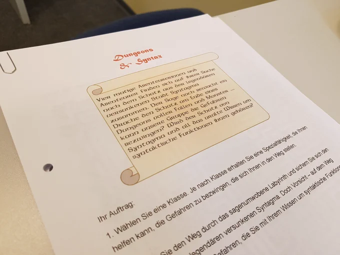 Ausgedruckte Arbeitsblätter zu Dungeons and Syntax. Abgebildet ist eine Schriftrolle mit einer kleinen Hintergrundgeschichte zum sagenumwobenen Syntagma und die Vorbereitungsaufgaben zum Spielen