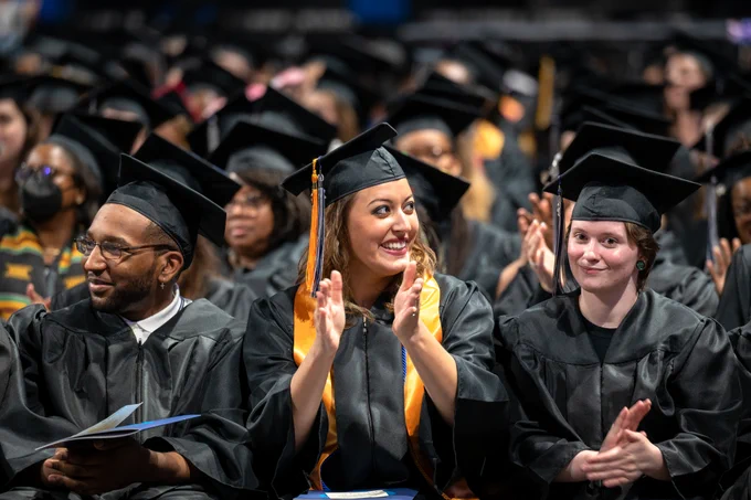 graduates clap while sitting in their chairs during the commencement ceremony