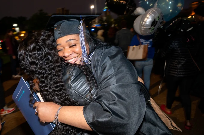 A female graduate tightly hugs a family member after graduating
