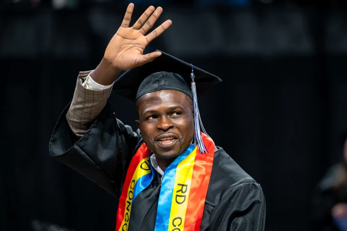 A male graduate waves to family in the crowd after crossing the stage