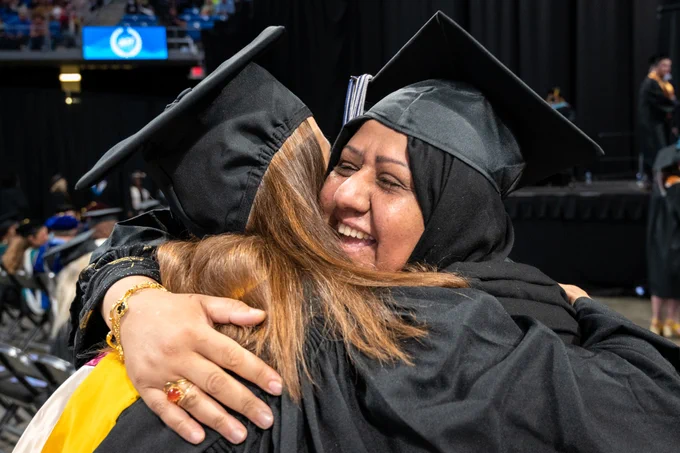 Two graduates joyously hug one another after crossing the stage