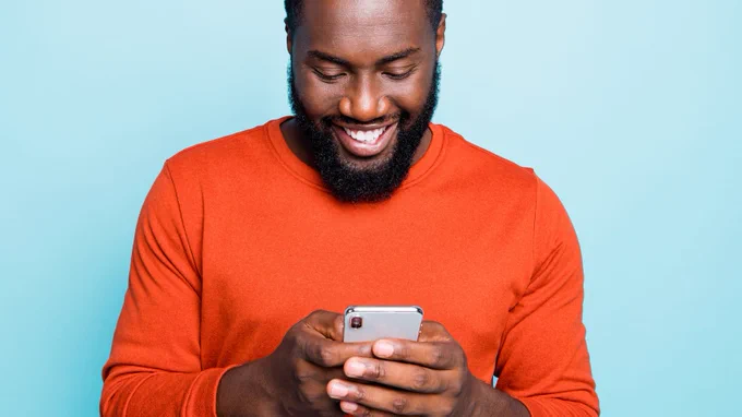 Adult male smiling while looking down at smartphone