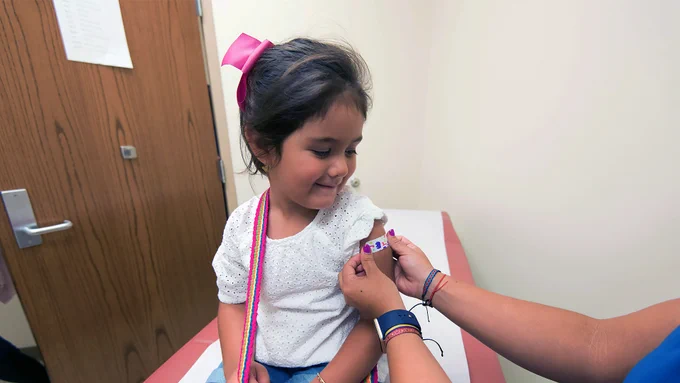 Young girl smiles and looks down as someone applies a plaster to her arm.