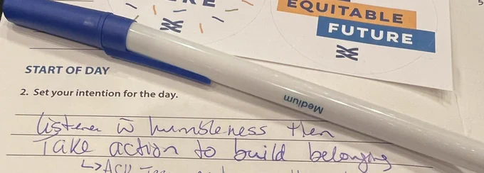 Paper and pen - paper says : Set your intention: Listen with humbleness then take action to build belonging.
