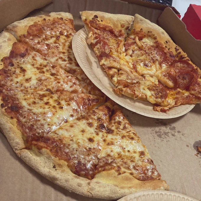 A plate of dominos pizza on a cardboard box. It looks delightfully greasy and cheesy.
