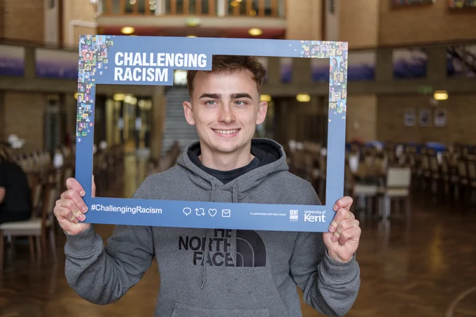 A Kent student smiling and holding up the Challenging Racism selfie frame 