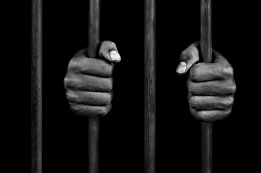 A hand holding the bars of a prison cell.