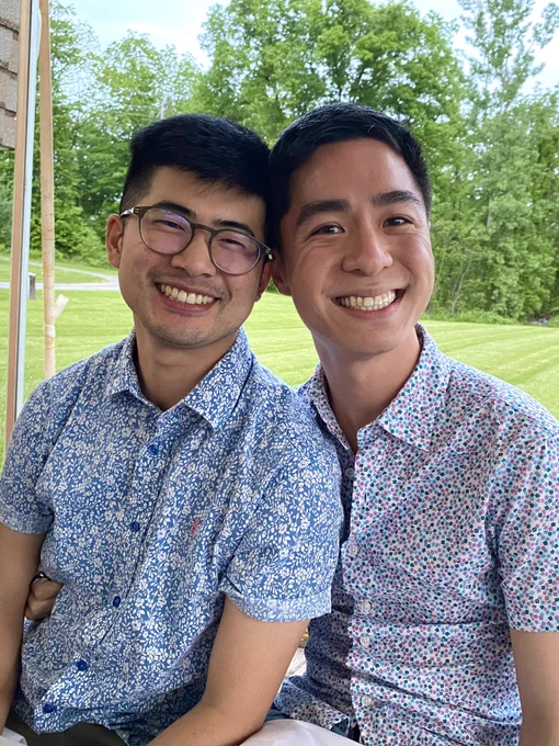 Aaron and I sitting together at our outdoor dining table at Dano’s. We are both wearing floral-patterned button down shirts and are smiling into the camera while our heads are placed next to each other. My hand is also wrapped around Aaron’s waist.