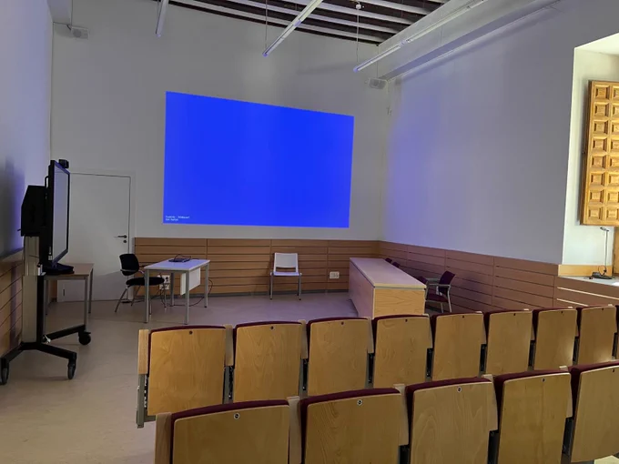 University room with a screen, a projector, several chairs, and two tables.