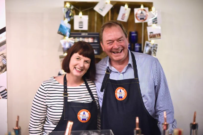 Sian & Andrew from Gower Gin wearing branded aprons smiling at the camera at their stand