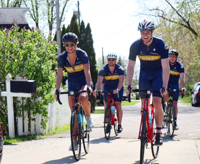 Four cyclists wearing ESTEEM team uniforms ride their bicycles along a quiet street during the 2022 Bike Ride for a Cure.