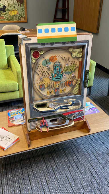 A ski-themed pachinko machine on a coffee table in the Director’s office at the Downtown Library. Armchairs and a mural in the background.
