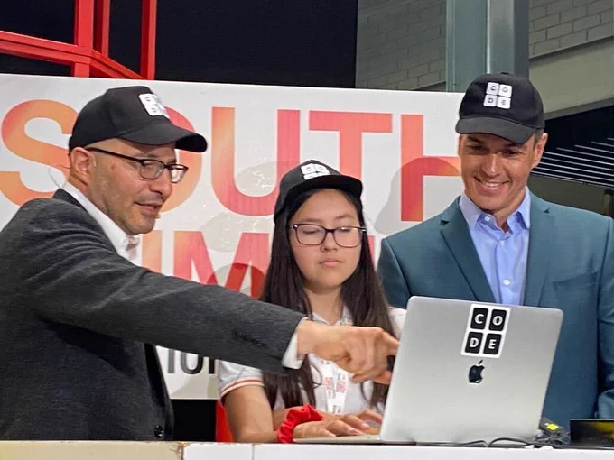 From left to right, Code.org co-founder Hadi Partovi, a student, and the President of the Spanish Government, Pedro Sánchez, stand at a laptop and participate in an Hour of Code.