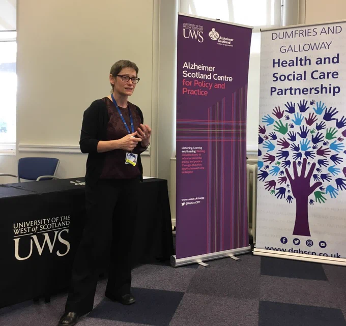 Wendy Chalmers is speaking with signs nearby for UWS, ASCPP and D&G Health and Social Care Partnership