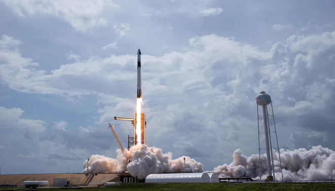 SpaceX rocket launching against a blue cloudy sky.