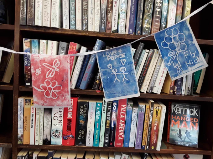 3 flags hanging in front of bookcase, their messages are: Love peace, Fly High, and a picture of a flower and dragonfly