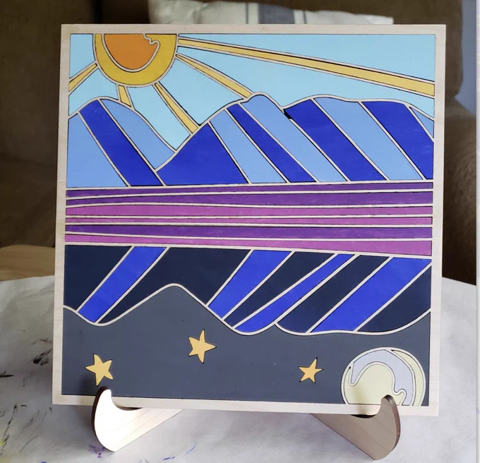 A 7.5" by 7.5" wood painted mosaic of a mountain scene featuring a daytime/nightime reflection.