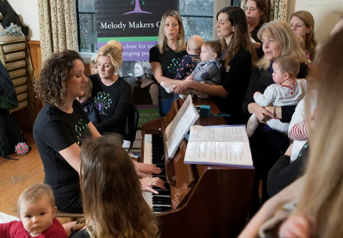 A group of parents sing around a piano