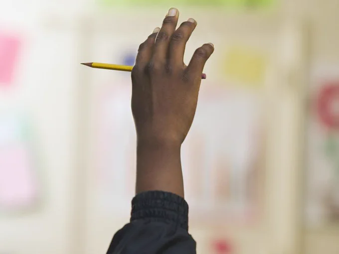 Child’s hand up in school with a pencil
