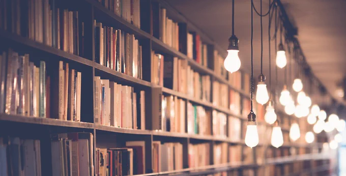 Floor-to-ceiling bookshelves with a string of bare lightbulbs hanging down in front of them.