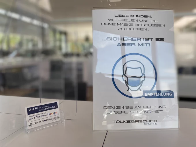 Schild mit der Aufschrift: Liebe Kunden, Wir freuen uns Sie ohne Maske begrüßen zu dürfen. … Sicherer ist es aber mit! (Empfehlung) Denken Sie an Ihre und unsere Gesundheit. Tölke Fischer Gruppe