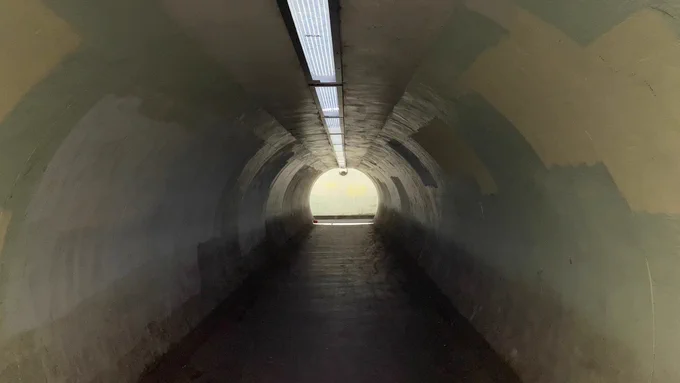 We are under the road in a long tunnel. You can see the light at the end of the tunnel. No people, just tunnel