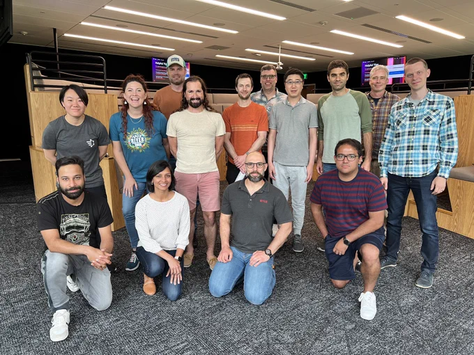 14 nerds stand or sit in two rows in a large conference room.