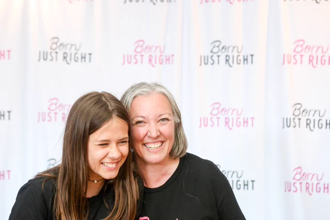 Jordan and Jen smile in front of a step and repeat in 2019 that says “Born Just Right” many times in purple and black.