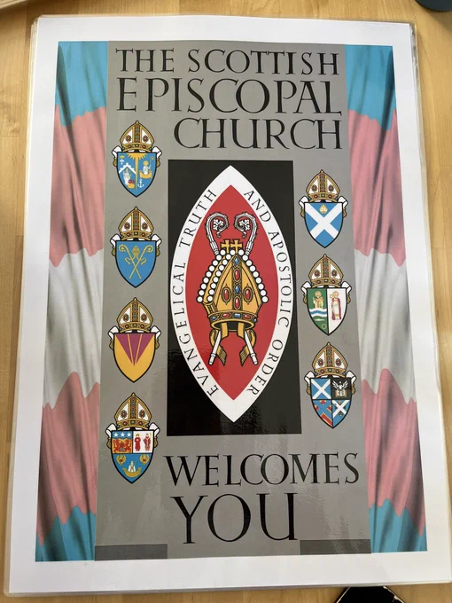 A placard reads The Scottish Episcopal Church Welcomes You on a background in the colours of the trans flag.