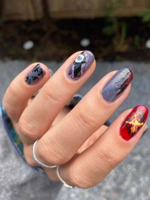 Close up of Stranger things season four nail art on a left hand in front of gray gravel. From pinky to thumb, gray background with black spiders, grandfather clock from the upside down on a gray background, a gray background of the upside down with a red crack that leads to Hawkins, the orange/yellow/red/black portal that leads to Hawkins, and green/white/gold stripes with the red cracks of the upside down portal.