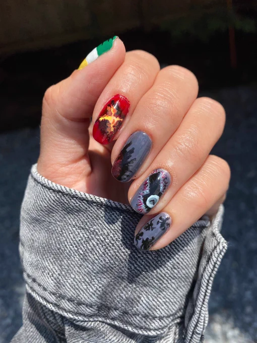 Stranger things season four nail art on a left hand in a fist in front of gray gravel. From pinky to thumb, gray background with black spiders, grandfather clock from the upside down on a gray background, a gray background of the upside down with a red crack that leads to Hawkins, the orange/yellow/red/black portal that leads to Hawkins, and green/white/gold stripes with the red cracks of the upside down portal.