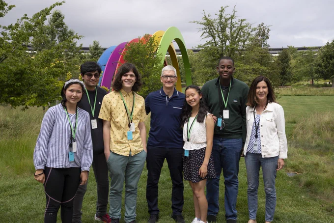 Tim and Susan Prescott stand with five of the Swift Student Challenge winners in front of the rainbow at Apple Park.