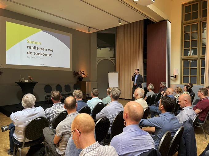 Zo'n twintig mannen kijken naar een presentatie met als titel "Samen realiseren we de toekomst"