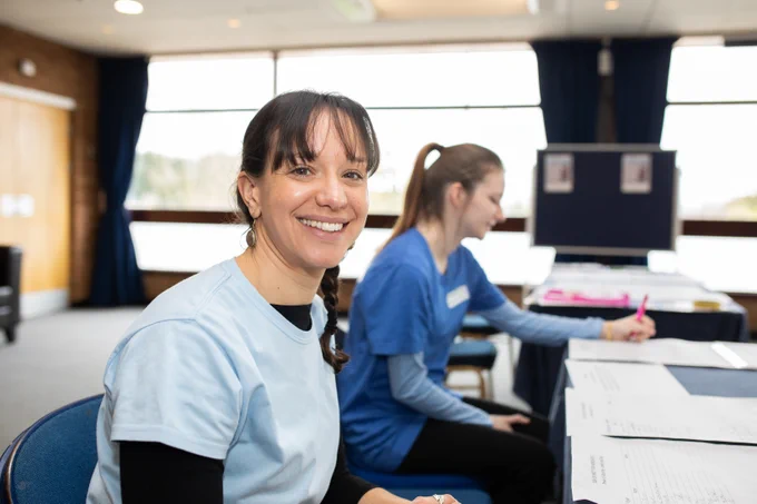 Two medical staff sit at a table. One smiles at the camera.