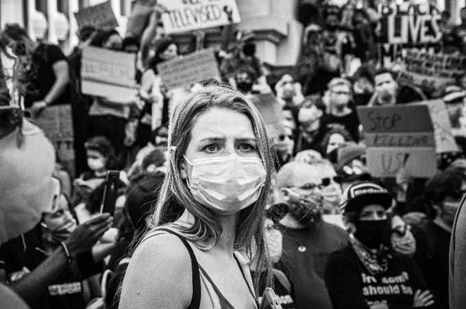 Protesters at Black Lives Matter march 2020 with placards with masked white woman in foreground