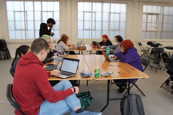 Team HEB and Team Jaguar on their own tables, collaborating with their team members, with snacks on their tables. A member from another team can be seen half-cropped in the right-hand-side of the view. 