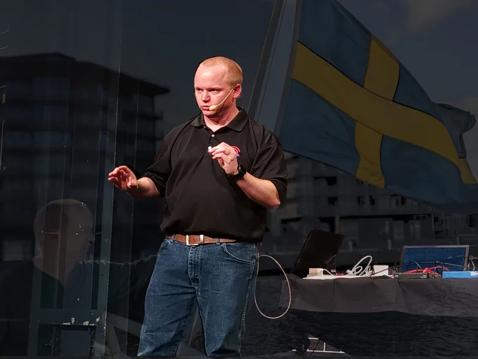 Dan presenting at Security Fest with Sweden's flag in the background