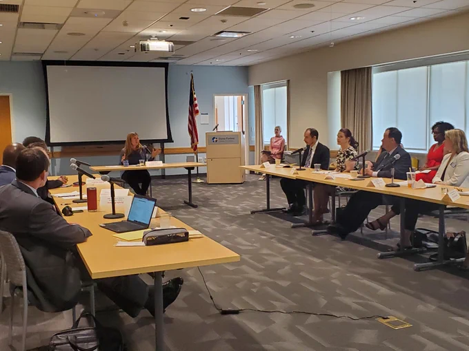 A conference room with people sitting around long tables and Kathi Vidal speaking at the head table
