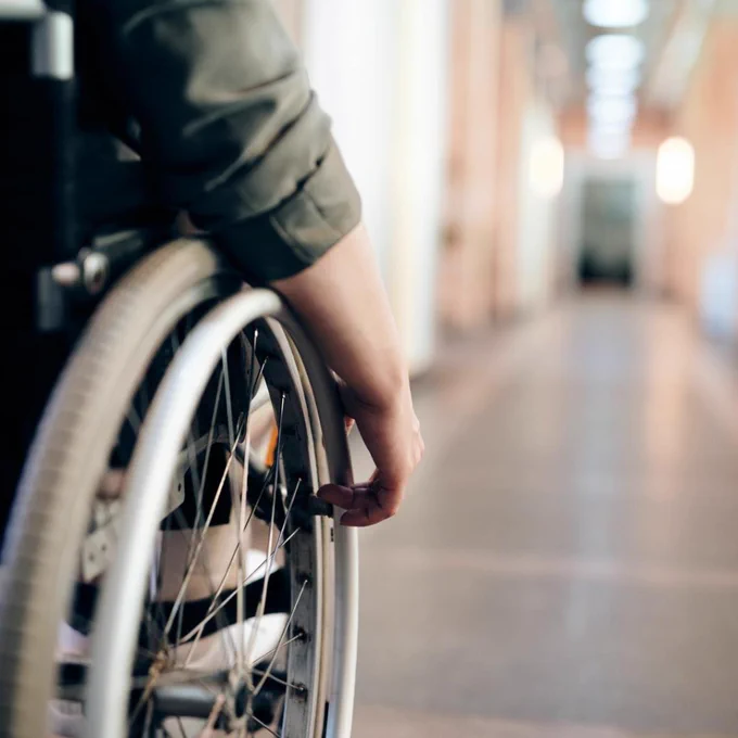 Close-up of a person in a wheelchair navigating a long hallway.