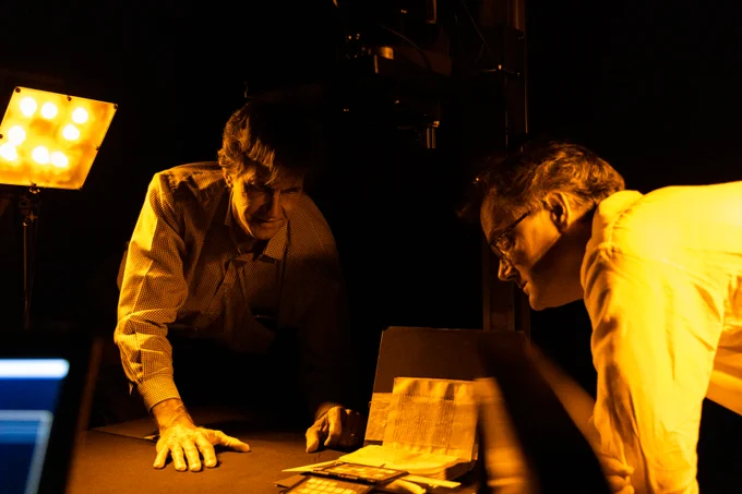 Mike Toth and Will Noel inspect an item under amber light. 