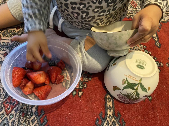 My toddler holding the small, chipped bowl on one hand and eating fruits with her other hand. Big bowl is upside down on the carpet!