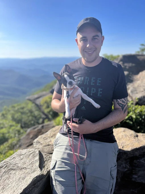 Jon leaning against rock wall, holding Freya with North Carolina mountains in background