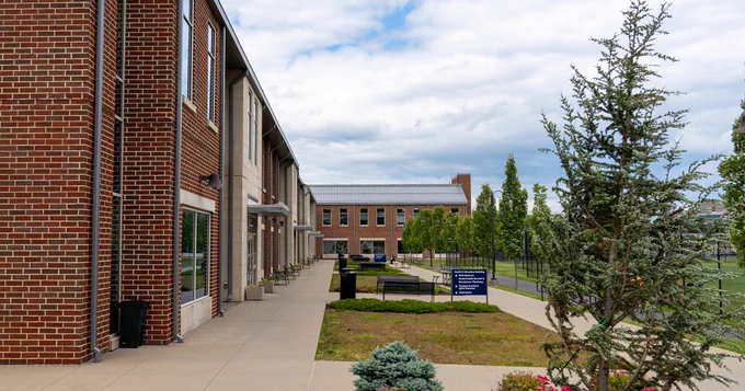 View of the WVU Student Wellness building showing the CPASS wing in the far end, with white clouds and blue skies above. 