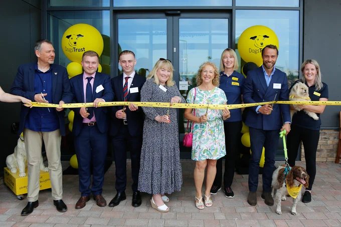 A yellow ribbon is being cut by eight people outside Dogs Trust Cardiff.
