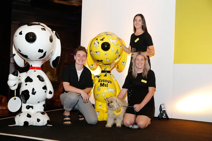 Three people pose with two Snoopy sculptures.