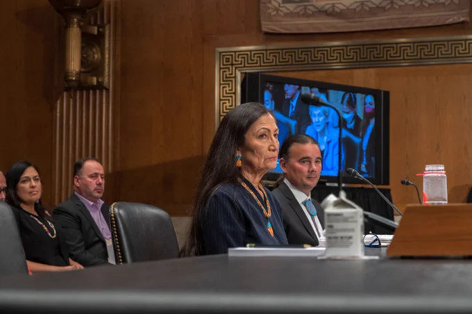 Secretary Haaland and Assistant Secretary for Indian Affairs Newland are seated at a table, listening to committee members of the Senate Indian Affairs Committee. 