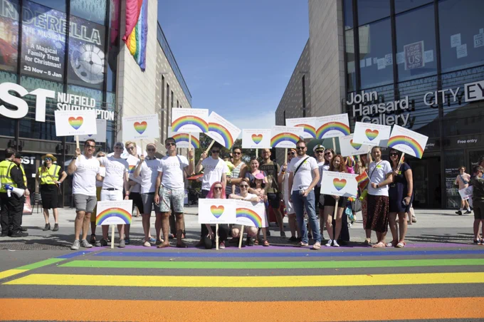 Solent University staff, students and alumni proudly supporting Southampton Pride, holding rainbow Solent placards in the city centre. In the background is the rainbow crossing, MAST Studio and John Hansard Gallery.