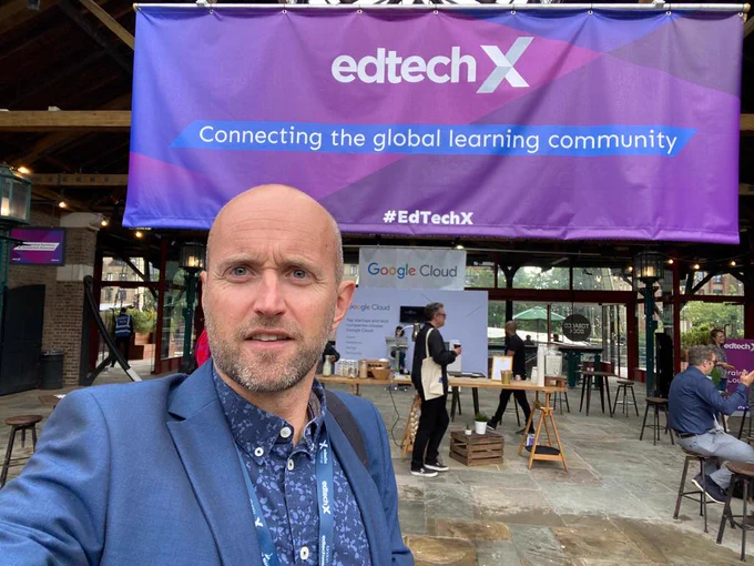 youHQ CEO Jon stands in front of a purple sign. The sign reads 'edtechX, connecting the global learning community. #edtechX' 